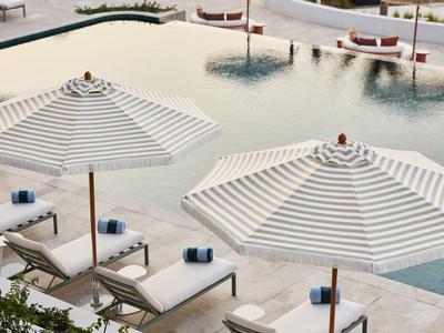 Zwei Liegestühle unter gestreiften Sonnenschirmen neben einem Pool auf einer Hotelterrasse.