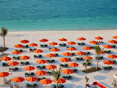 Strand mit vielen orangefarbenen Sonnenschirmen und Palmen am blauen Meer.