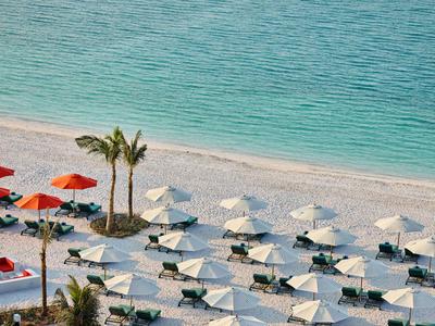 Strand mit Reihen von weißen Sonnenschirmen und Liegestühlen neben blauem Meer