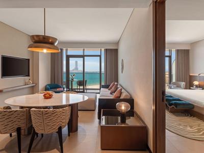 Moderní hotelový pokoj s jídelním koutem, pohovkou a balkonem s výhledem na moře.