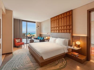 Modernes Hotelzimmer mit großem Bett, Sitzbereich und Meerblick durch das Fenster.