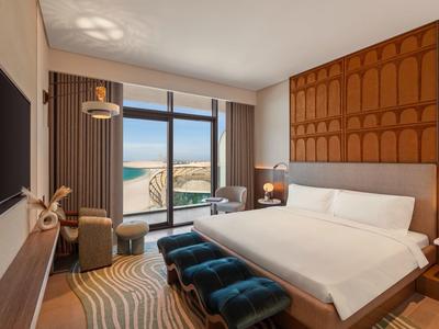 Moderní hotelový pokoj s velkou postelí, panoramatickým oknem a výhledem na pobřeží.