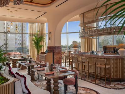 Elegantní hotelový bar se stylovým dřevěným nábytkem a velkými okny, která propouštějí denní světlo.