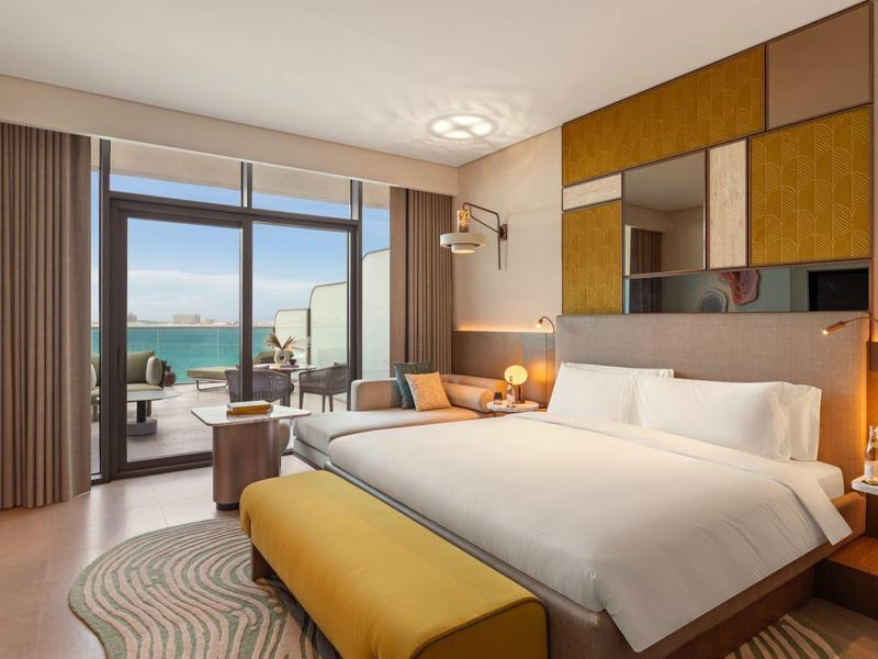 Moderní hotelový pokoj s manželskou postelí, velkým oknem a výhledem na moře.