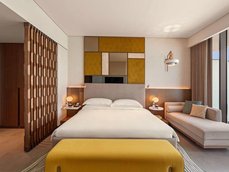 Moderní hotelový pokoj s manželskou postelí, lounge sedačkou a velkým balkonem s výhledem na moře.