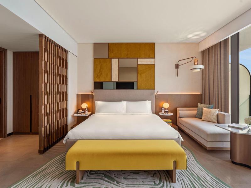 Moderní hotelový pokoj s velkou postelí, žlutou lavicí, pohovkou a panoramatickým výhledem.