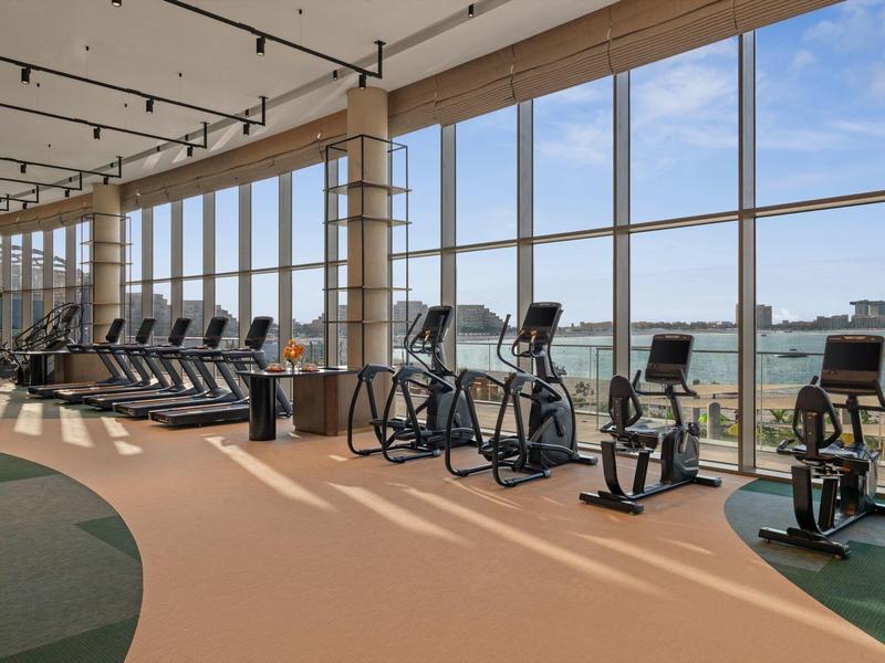 Světelné fitness s výhledem na vodu a město skrz velká okna.