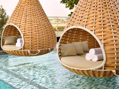 Zwei hängende, Korb-förmige Betten am Pool mit Kissen und Handtüchern.