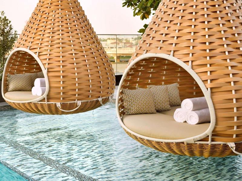 Zwei hängende, Korb-förmige Betten am Pool mit Kissen und Handtüchern.