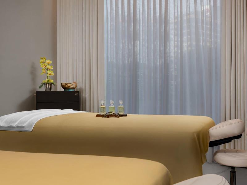 Ein ruhiger Massageraum mit zwei Liegen und einem Fenster mit transparenten Vorhängen.