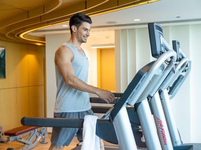 Uomo che si allena su un tapis roulant in una palestra moderna con grandi finestre.