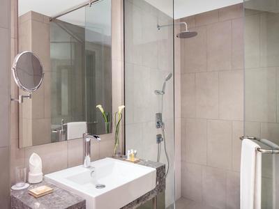 Moderní koupelna se čtvercovým umyvadlem, skleněným sprchovým koutem a osvětleným zrcadlem.