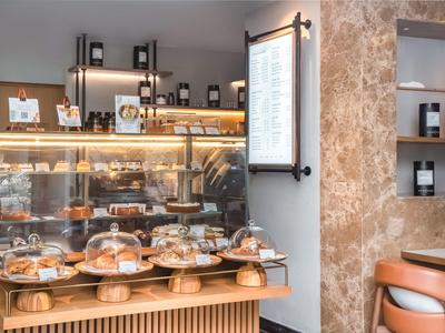 Moderní kavárna se skleněnou vitrínou plnou zákusků a pečiva na dřevěném pultu.