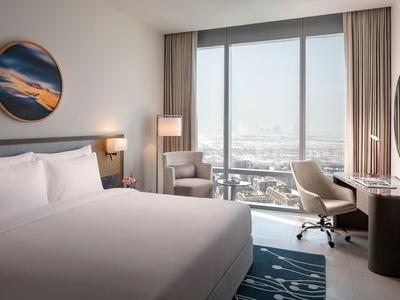 Moderní hotelový pokoj s velkým oknem, postelí, židlemi a psacím stolem se zrcadlem.