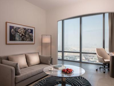 Elegantní obývací pokoj se šedou pohovkou, kulatým skleněným stolem a velkým panoramatickým oknem s výhledem na město.