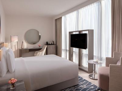 Moderní hotelový pokoj s velkou postelí, TV před oknem a útulným posezením.