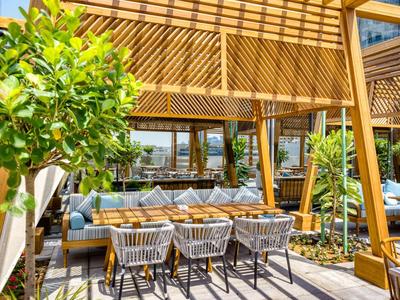 Moderne Terrasse mit Holzpergola, Sitzbereich und Essbereich umgeben von Pflanzen.
