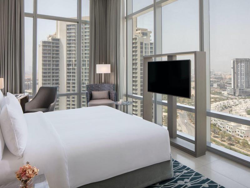 Moderně zařízený hotelový pokoj s velkou postelí a panoramatickými okny s výhledem na město.