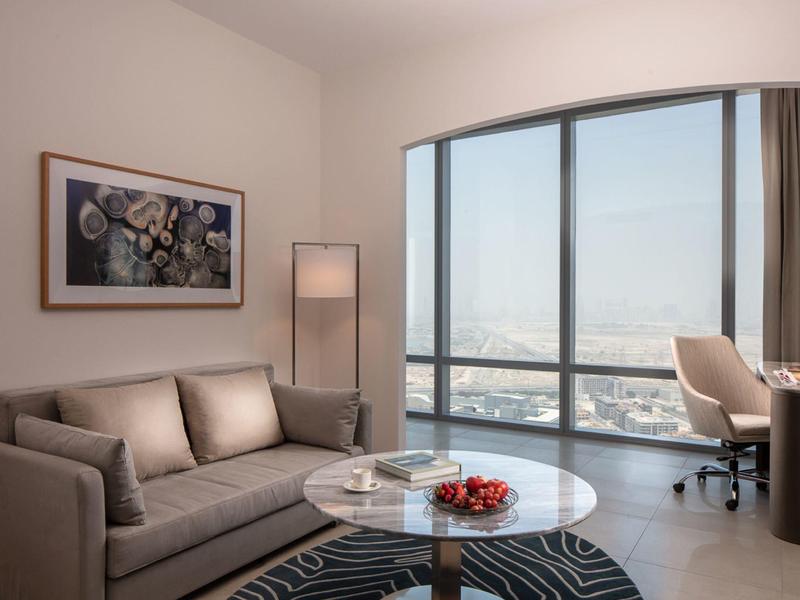 Elegantní obývací pokoj se šedou pohovkou, kulatým skleněným stolem a velkým panoramatickým oknem s výhledem na město.