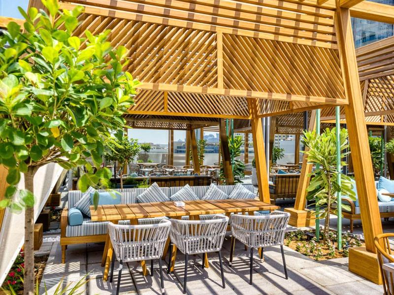 Moderní terasa s dřevěnou pergolou, posezením a jídelními místy obklopená rostlinami.