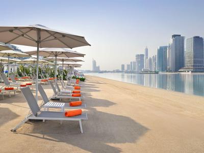 Strandliegen mit orangen Handtüchern unter Sonnenschirmen am ruhigen Stadtstrand.