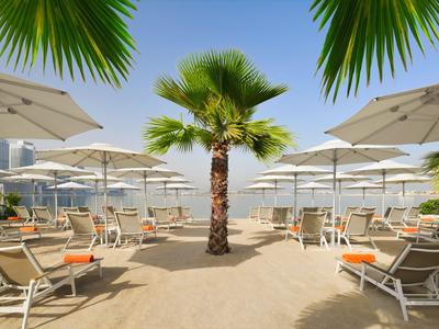 Strand mit Liegestühlen, Sonnenschirmen und Palmen unter klarem Himmel