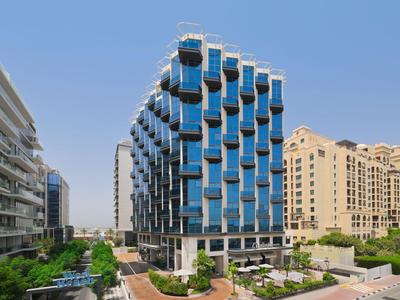 Moderner mehrstöckiger Hotelbau mit reflektierenden Glasbalkonen in urbaner Umgebung bei klarem Himmel.