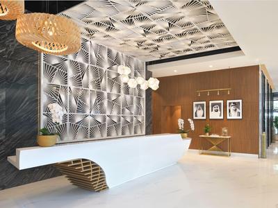 Moderner Hotellobby-Empfang mit weißem Tresen, geometrischer Wand und hängenden Lampen.