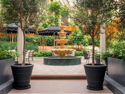 Courtyard with fountain, trees in large pots, and umbrellas in the background.