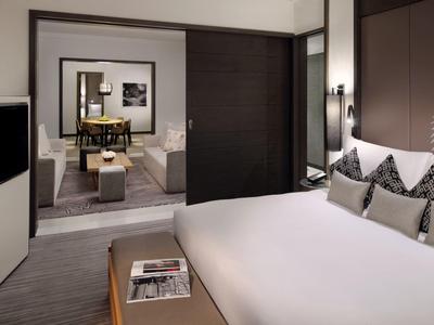 Modern hotel room with large bed, stylish decor, and view into living area.