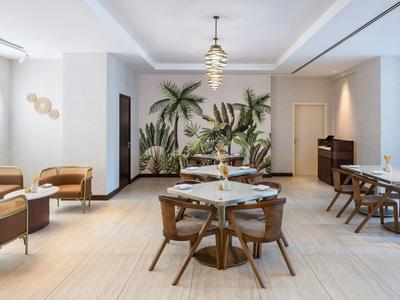 Modern hotel restaurant with plant wall, wooden tables, and beige chairs in bright rooms.