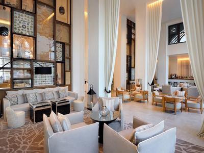 Bright, modern hotel lounge with high ceilings, curtains, and comfortable seating areas.
