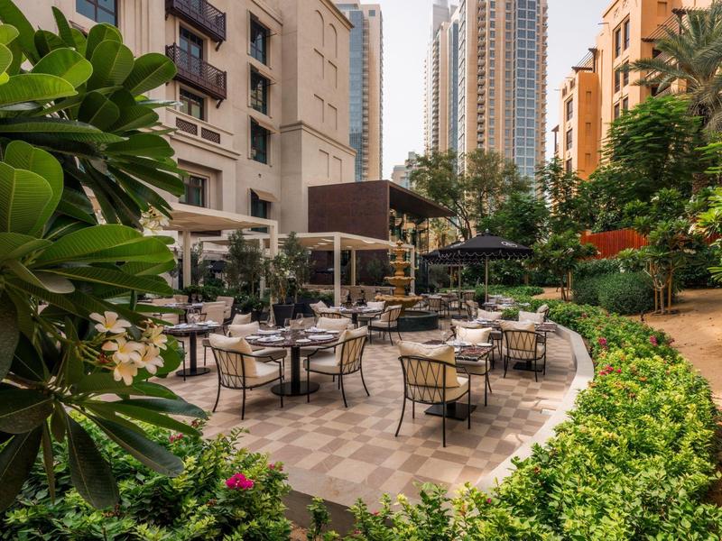 Outdoor seating area of a hotel surrounded by green plants and tall buildings.