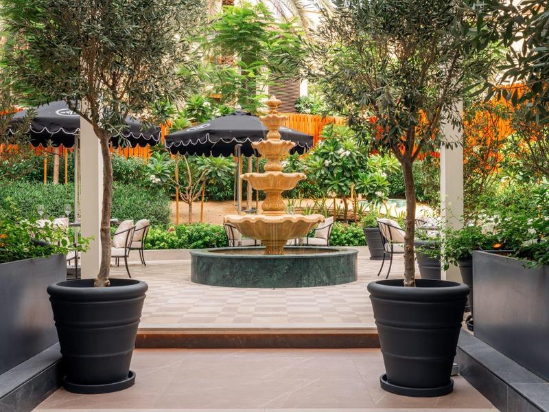 Courtyard with fountain, trees in large pots, and umbrellas in the background.