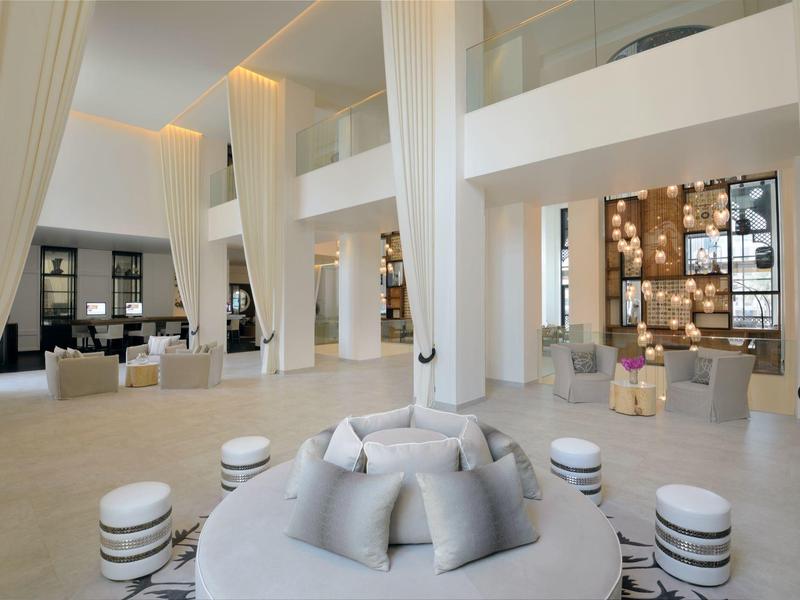 Bright hotel lobby with tall white columns, round seating areas, and elegant lighting.