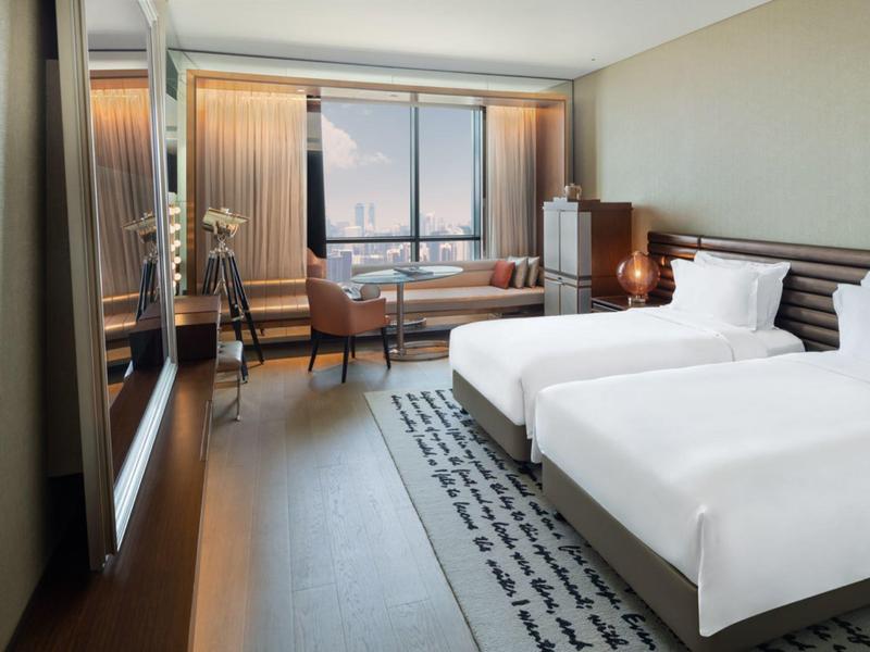 Helles Hotelzimmer mit zwei Einzelbetten, Sitzbereich und großem Fenster mit Ausblick.