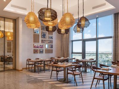 Elegantní restaurace s dřevěným nábytkem, velkými okny a moderními závěsnými svítidly.