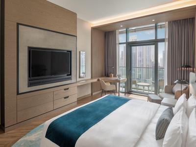 Modern hotel room with double bed, TV, and balcony overlooking the city.
