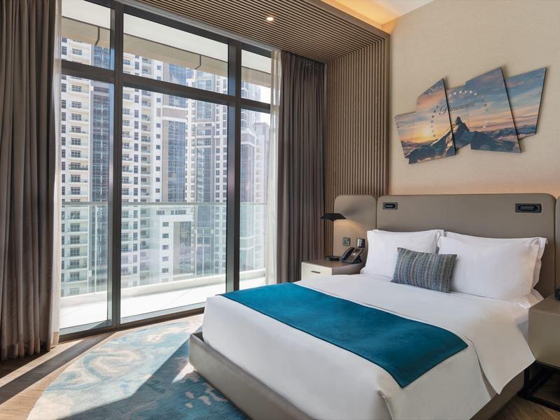 Modern hotel room with large window and city view, comfortable bed, and stylish decor.