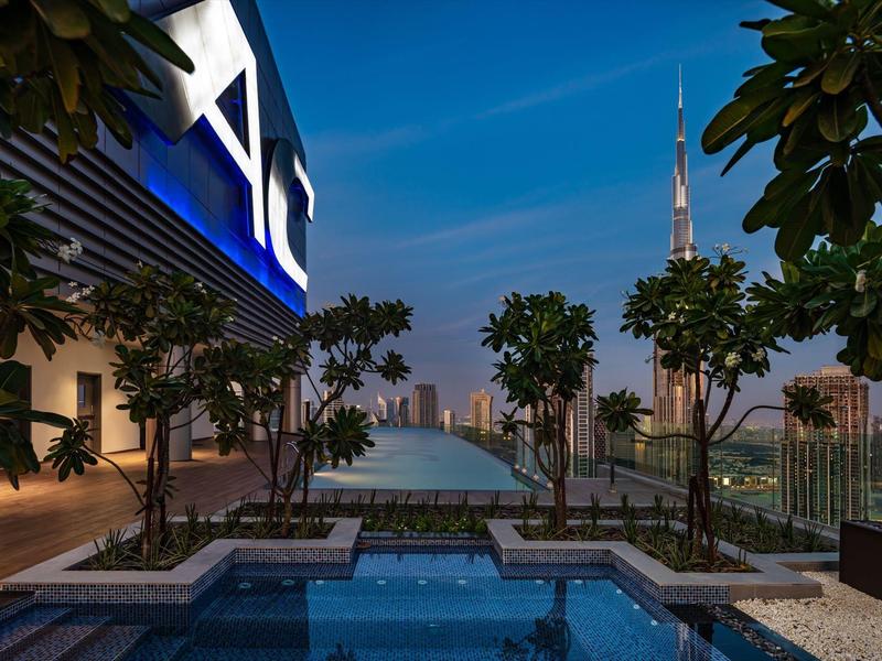 Luxurious rooftop pool area with city skyline and tall tower at sunset.