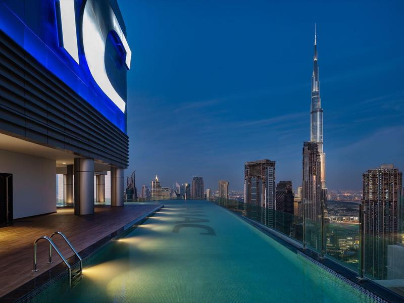 Infinity pool on rooftop terrace with view of illuminated skyline and Burj Khalifa at night.
