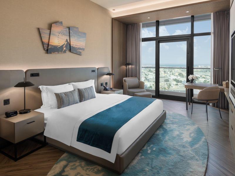 Modern hotel room with large bed, seating area, and panoramic window view.