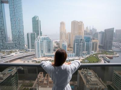Persoon kijkt vanaf balkon naar moderne wolkenkrabber skyline in stad met rivier.