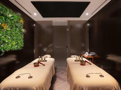 Twee massagetafels in een moderne spa-ruimte met groene wanddecoratie.