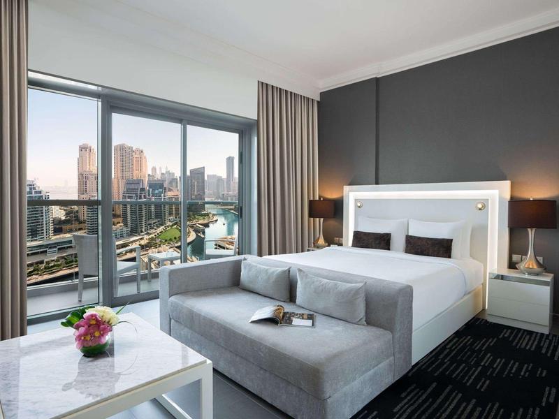 Moderne hotelkamer met groot bed, bank en uitzicht op de stad door grote ramen.