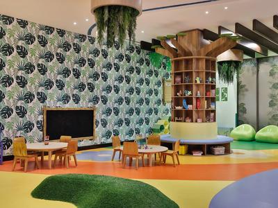 Salle de jeux pour enfants moderne et colorée avec petites tables, chaises et décorations vertes.