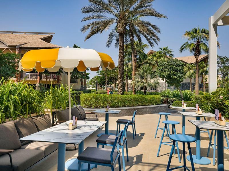 Espace extérieur moderne d'hôtel avec des chaises bleues, des tables et des plantes sous des palmiers.