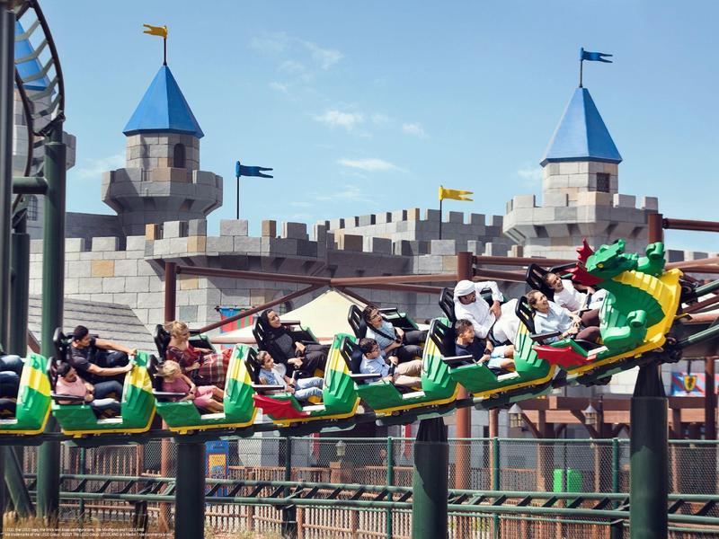Montagnes russes avec des wagons dragons verts devant un décor de château par temps clair.