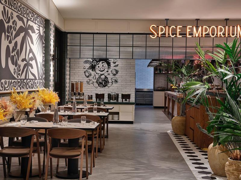 Restaurant moderne avec tables en bois, chaises, plantes et panneau visible 'Spice Emporium'