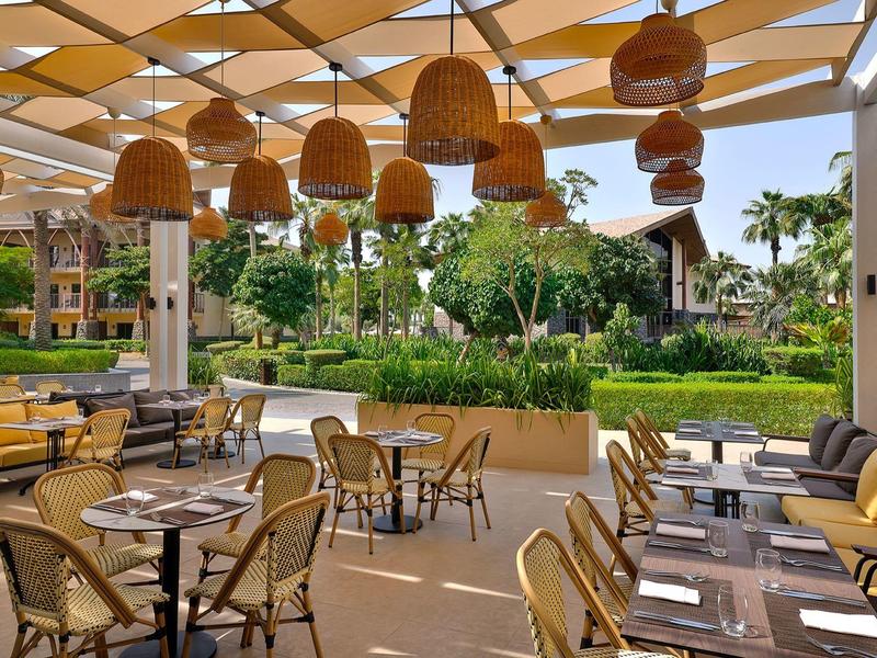 Espace extérieur couvert d'un hôtel avec tables, chaises et vue sur les jardins.
